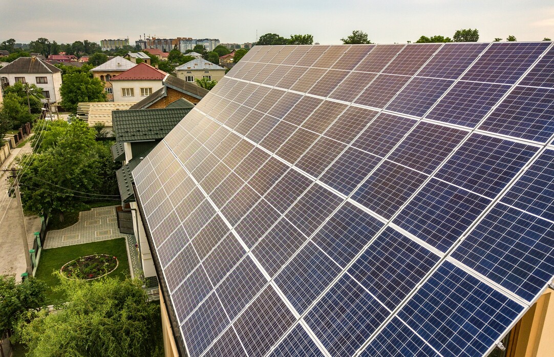 Zu sehen sind Solarmodule auf einem Hausdach in einem Wohngebiet, die Sonnenenergie zur Stromerzeugung nutzen.