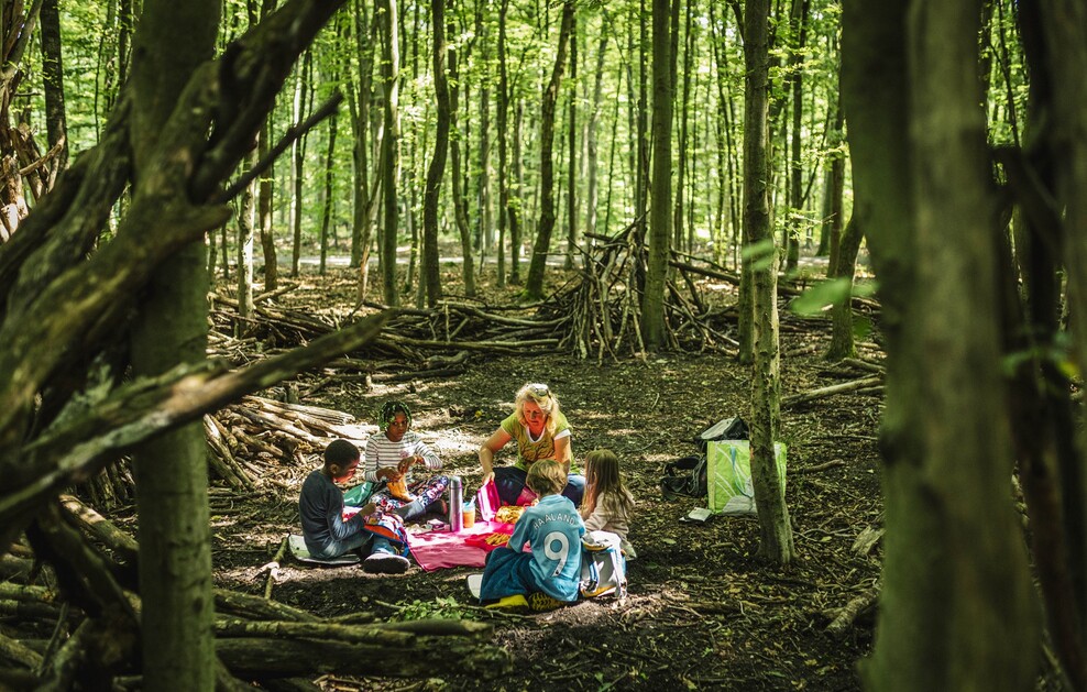 Szene im grün-dunklen Wald, eine Frau sitzt mit Kindern im Kreis