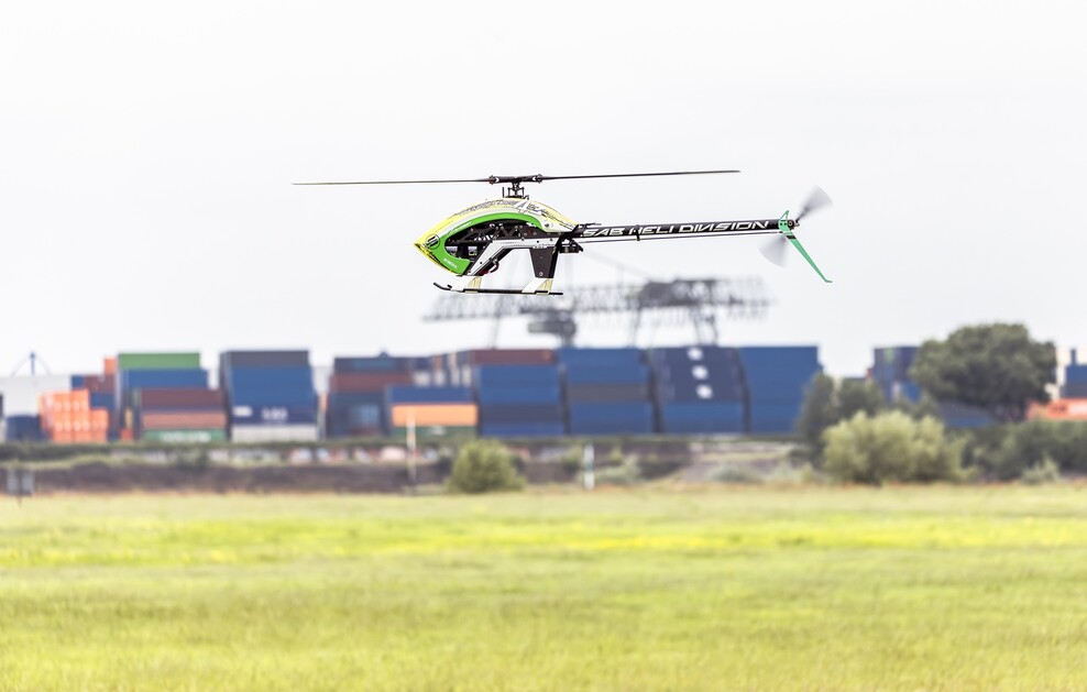 Aufnahme eines Modellflugzeugs über einer Wiese vor Industriekulisse