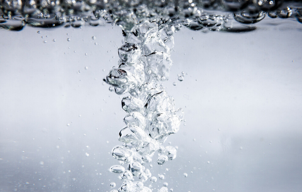 Blasen steigen in klarem Wasser auf, die Wasseroberfläche ist ebenfalls voller Blasen.