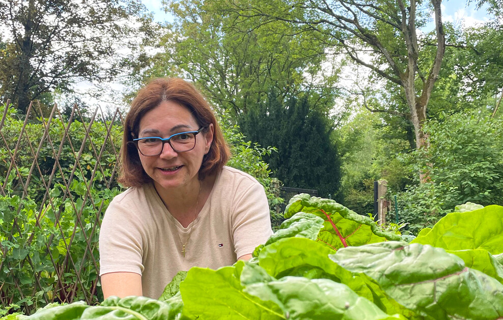 Eine lächelnde Frau mit Brille und schulterlangem, braunem Haar gärtnert in einem Hochbeet.