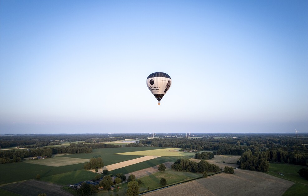Ein Heißluftballon schwebt über eine leicht hügelige Landschaft. Himmel in leichter Dämmerung.