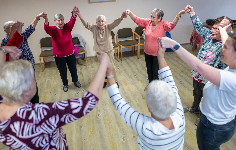 Eine Gruppe älterer Damen hält sich an den Händen und bildet dabei einen Kreis.